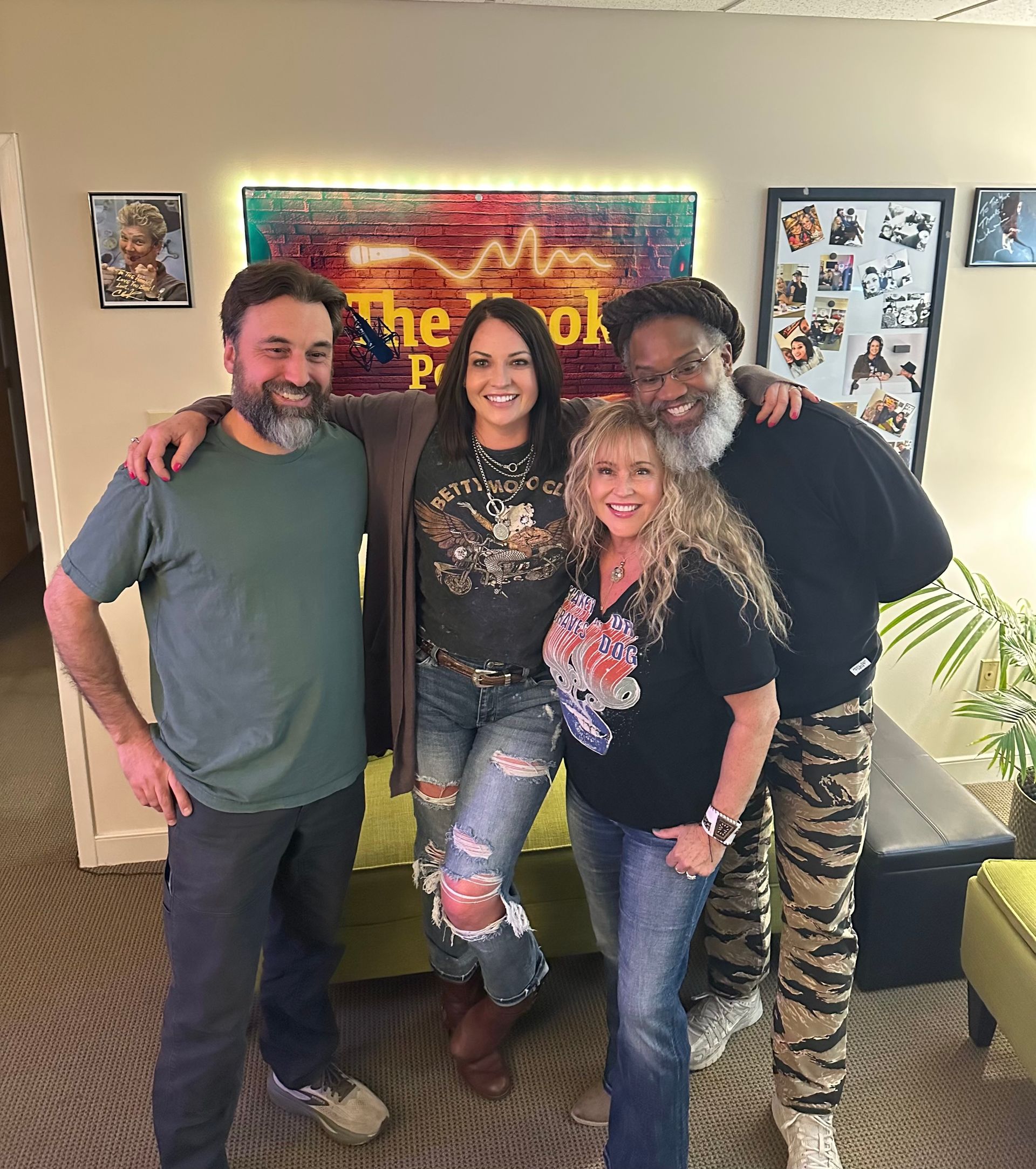 Four smiling people standing together indoors, posing in front of colorful wall art.