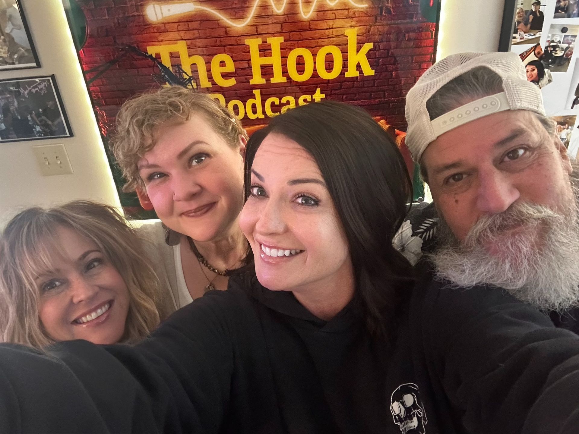 Four friends smiling for a selfie in front of a The Hook podcast sign