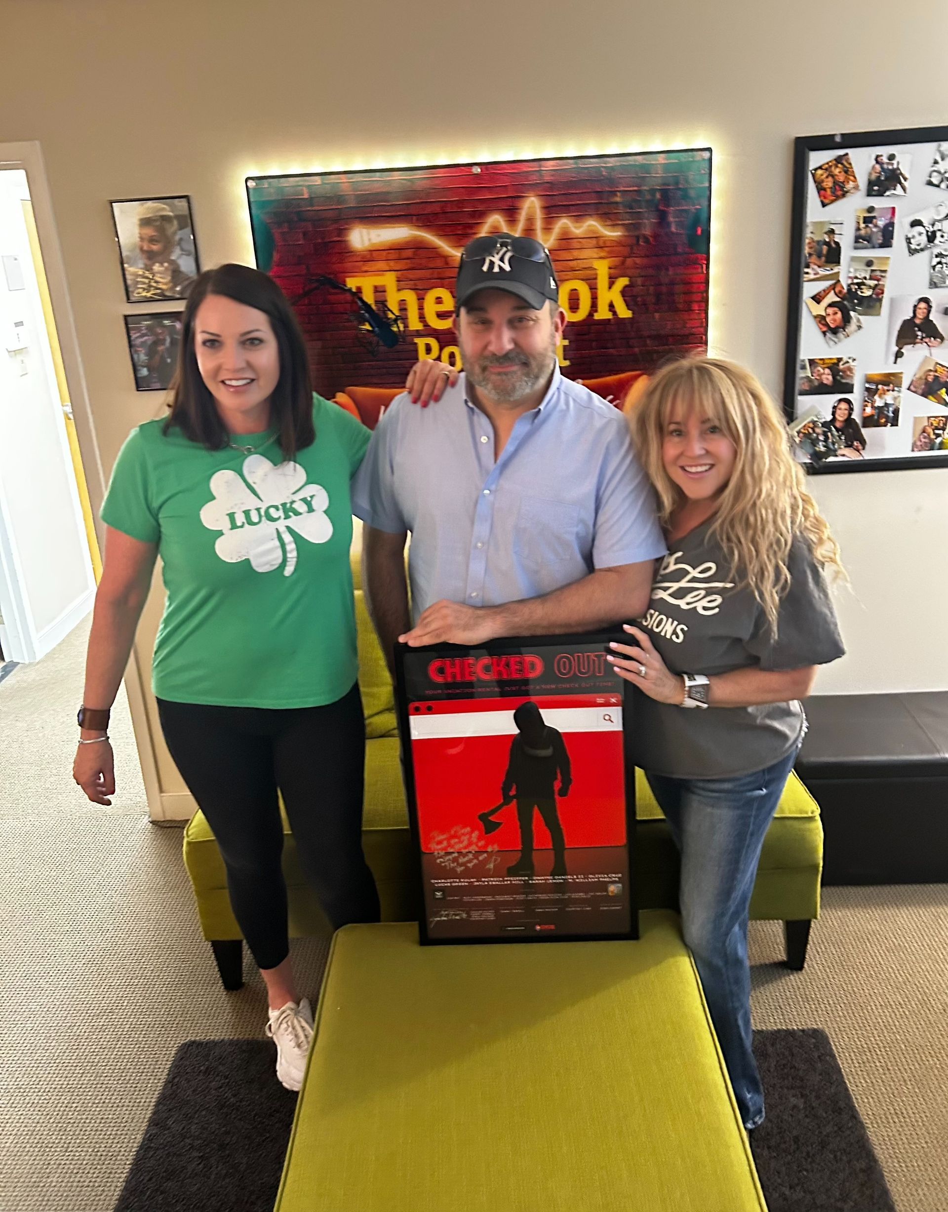 Three people smiling indoors, posing with a framed poster in front of a “The Cook” wall sign.