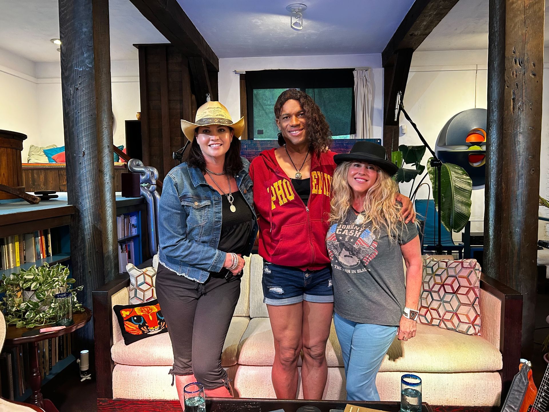 Three people posing in a living room, smiling and standing in front of a couch.