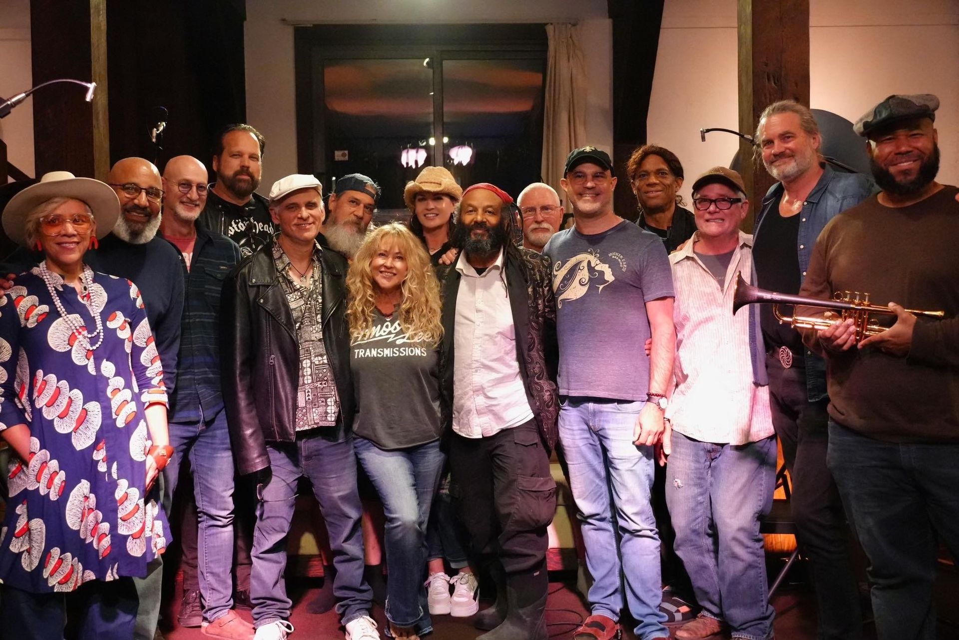 Group of people posing indoors, smiling and wearing matching casual outfits and hats on a stage-like set