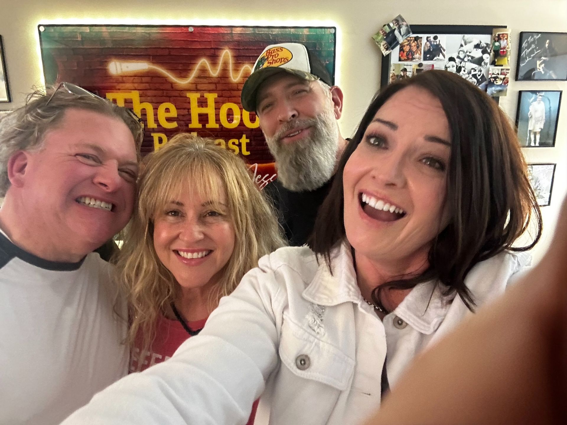 Four smiling people taking a selfie indoors, with framed wall art in the background.