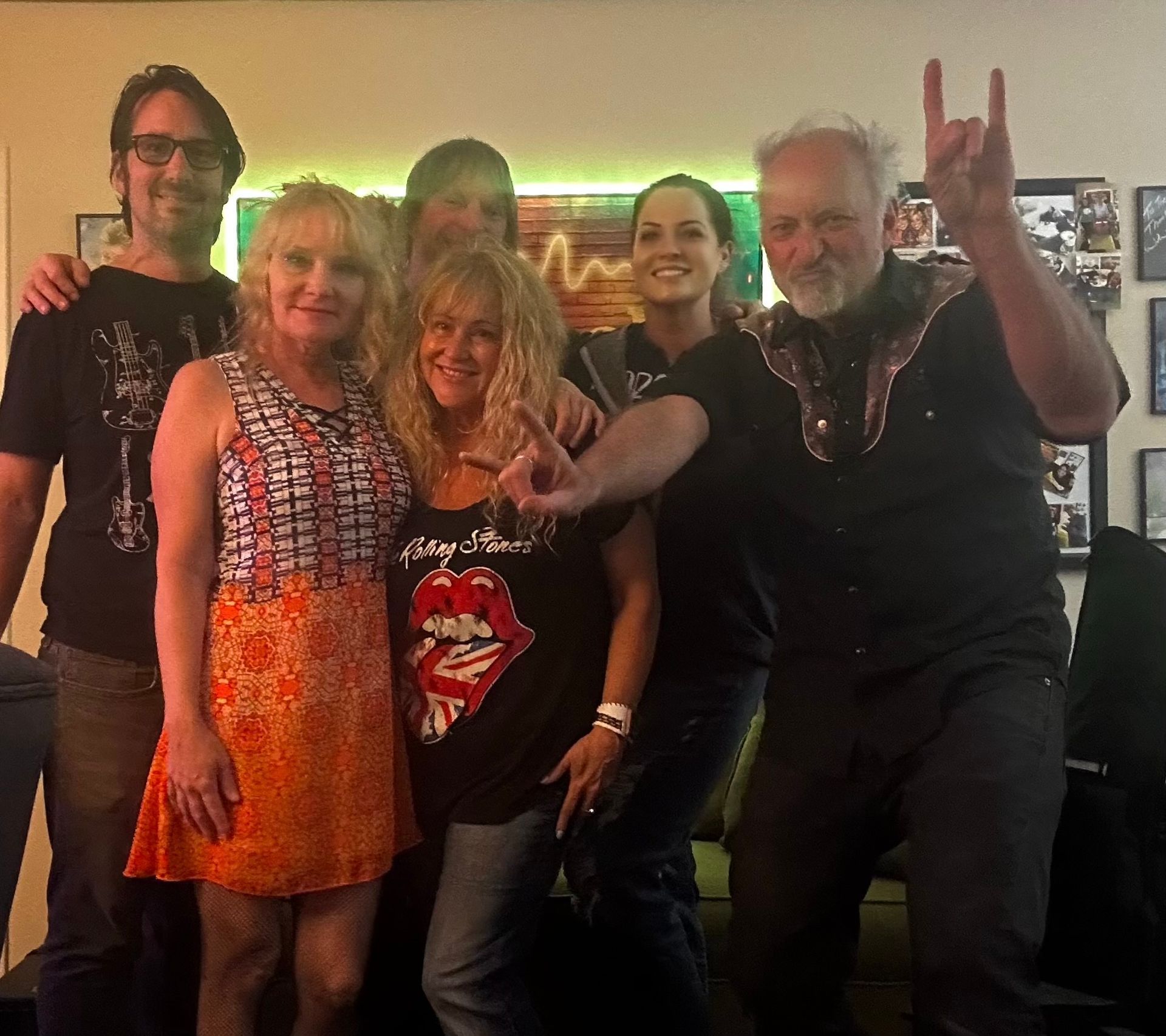 Five people posing together indoors, smiling and holding up rock hand signs.