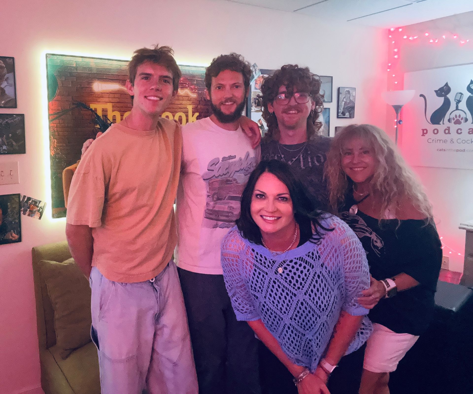 Five people posing together in a warmly lit room with neon wall art and colorful party decor.