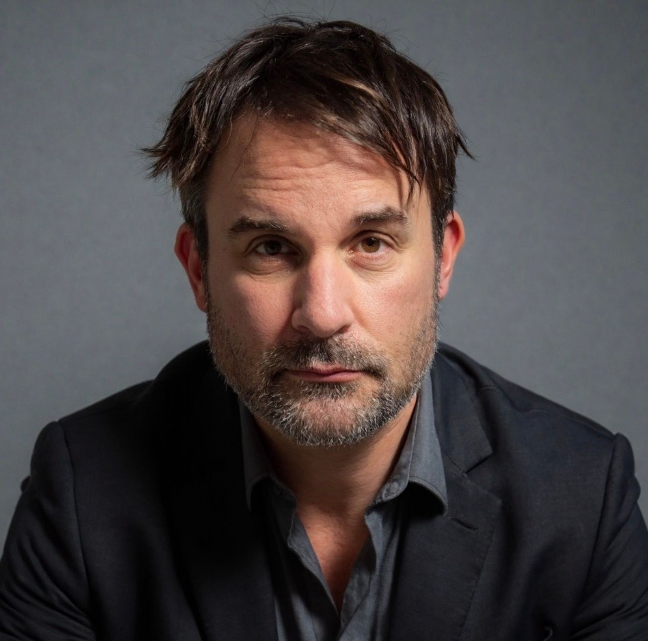 Studio headshot of a man in a dark blazer, looking at the camera with a neutral expression.