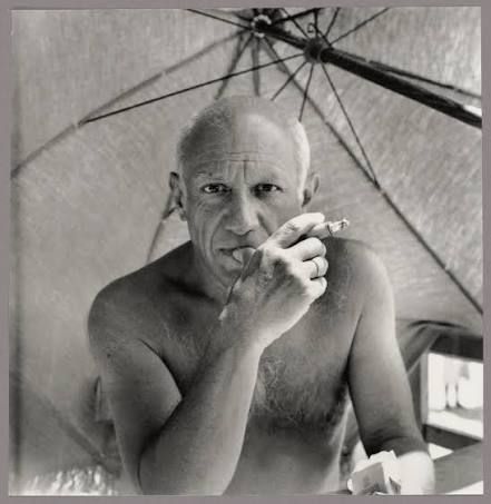 Black-and-white portrait of a shirtless man under an umbrella, holding a cigarette and looking at the camera