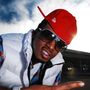 Man in red cap and sunglasses posing outdoors against a cloudy sky and building.