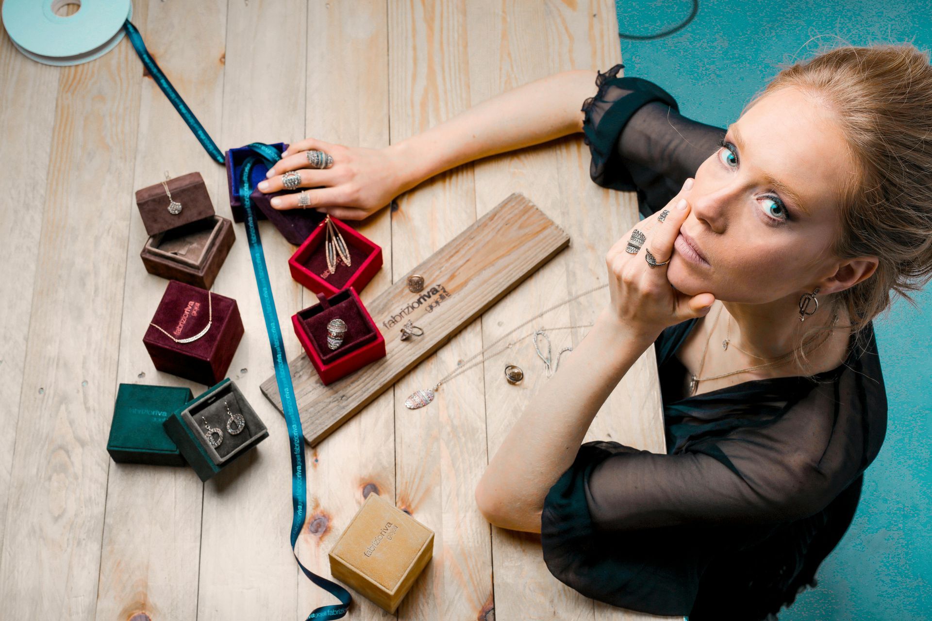 Woman surrounded by jewelry boxes and rings on a wooden table, looking up.
