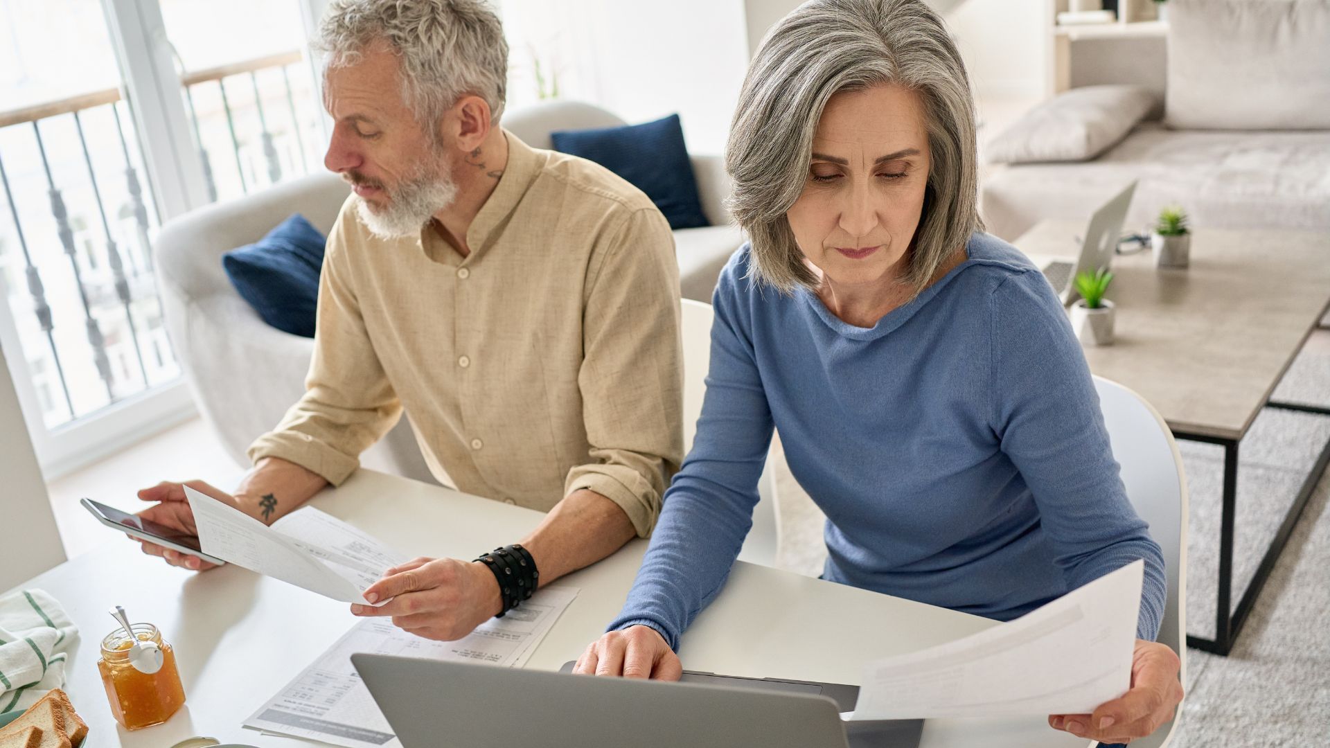 A man and a woman are sitting at a table looking at a laptop.