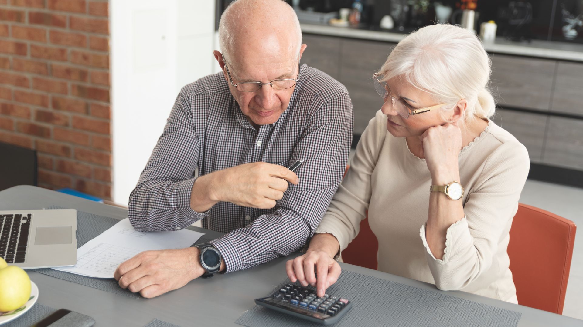 An elderly couple is sitting at a table using a calculator.