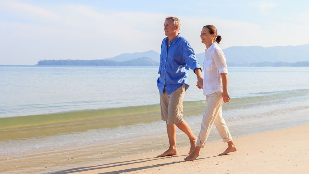 A man and a woman are walking on the beach holding hands.