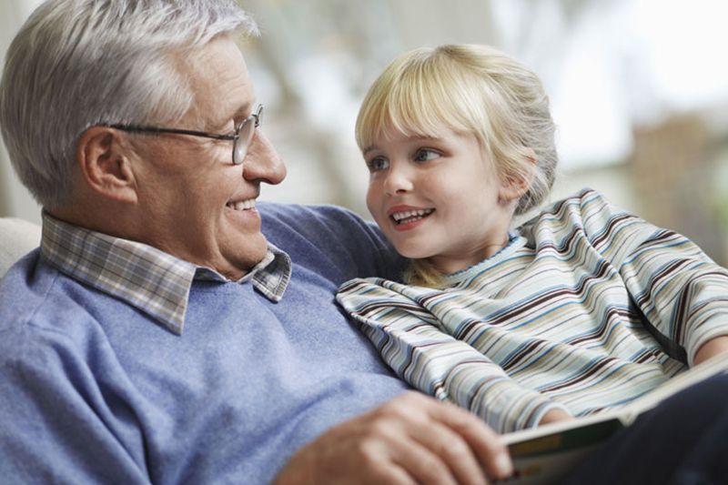 An elderly man is reading a book to a little girl.