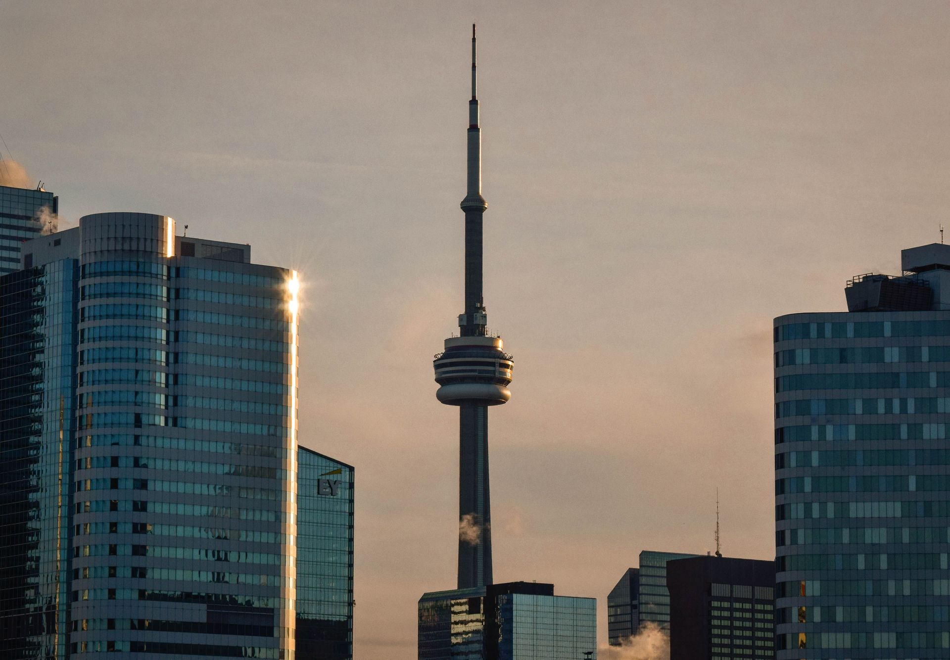 City skyline at sunset with the CN Tower centered between high-rise buildings.