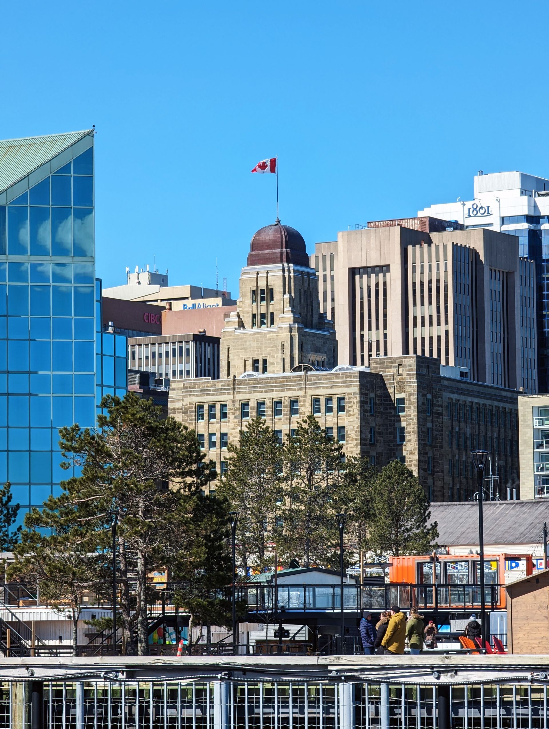 City skyline with a Canadian flag, glass tower, and historic stone building on a clear day