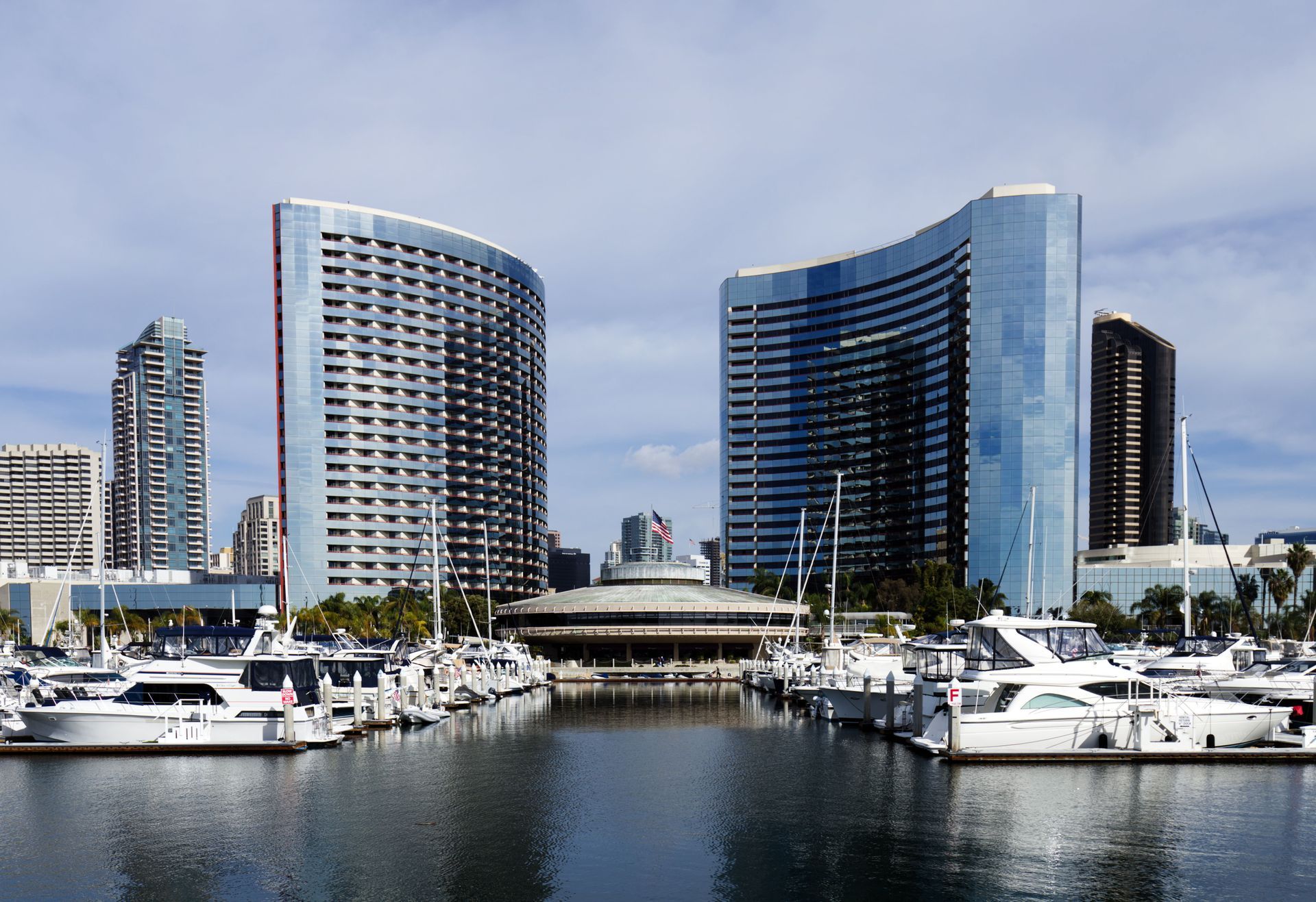 Marina with yachts in foreground and modern curved high-rise buildings along the waterfront.