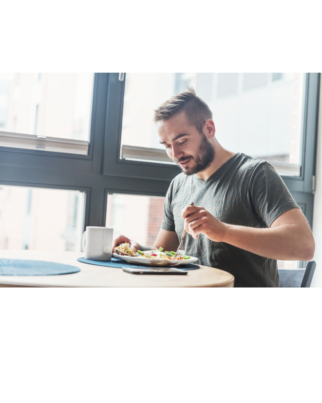 Man eating at a table, near a window, holding a fork.