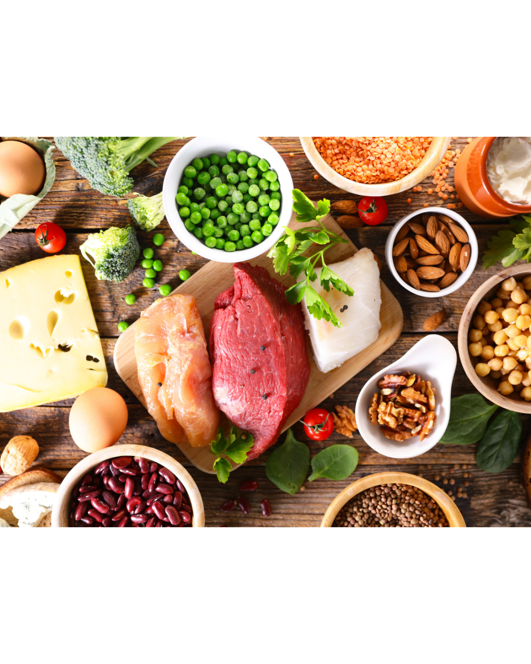 Assorted protein-rich foods, including meat, fish, eggs, beans, nuts, cheese, and vegetables, arranged on a wooden surface.
