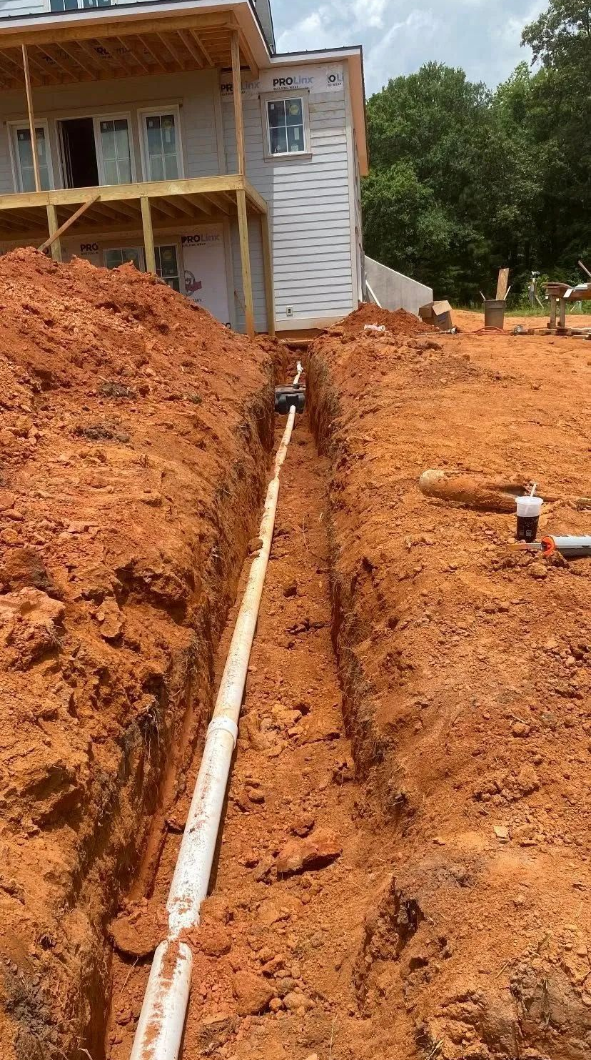 White drainage pipe in a red dirt trench beside a house under construction
