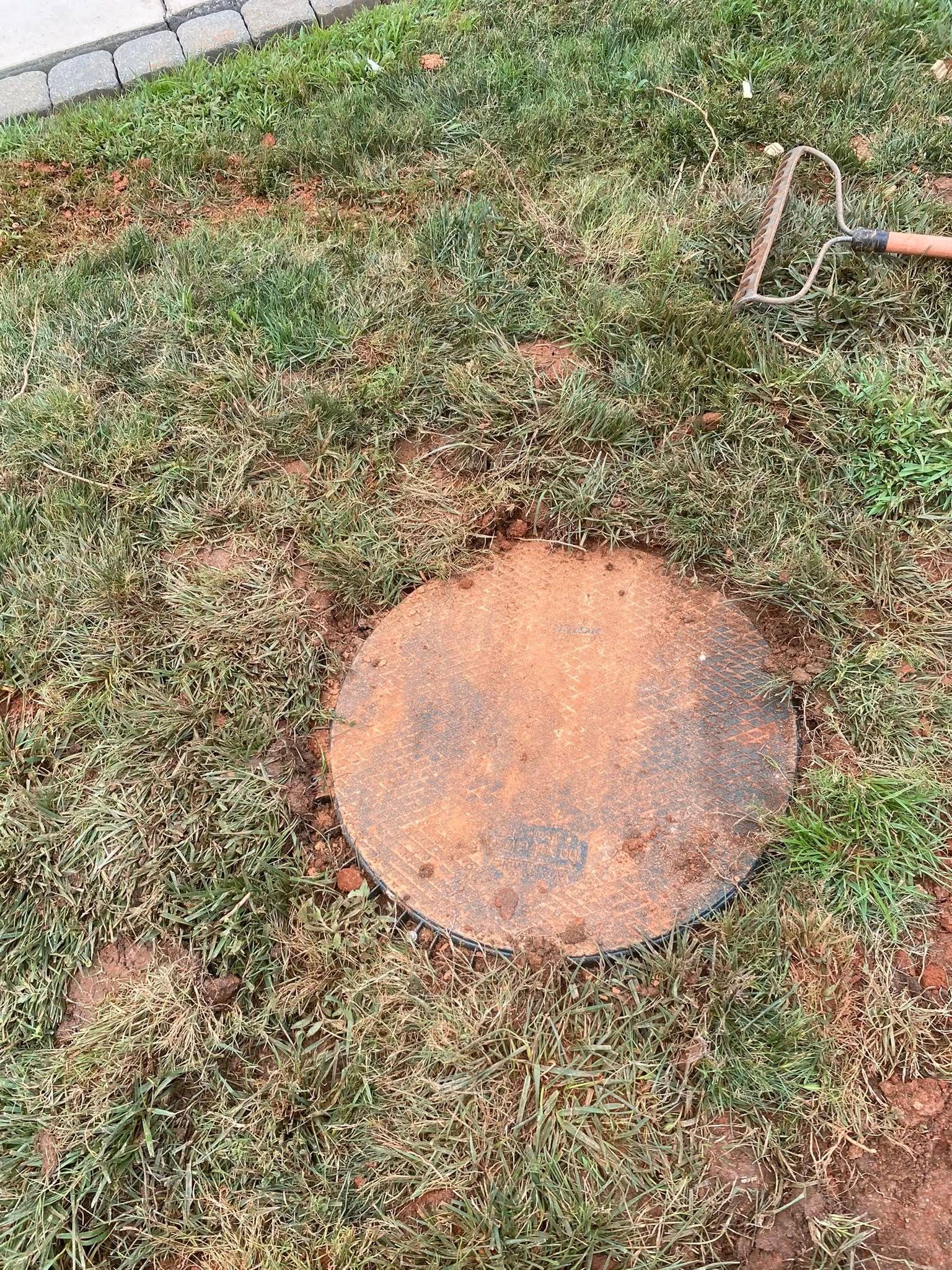 Round, rusty metal lid in a grassy yard, near a rake.