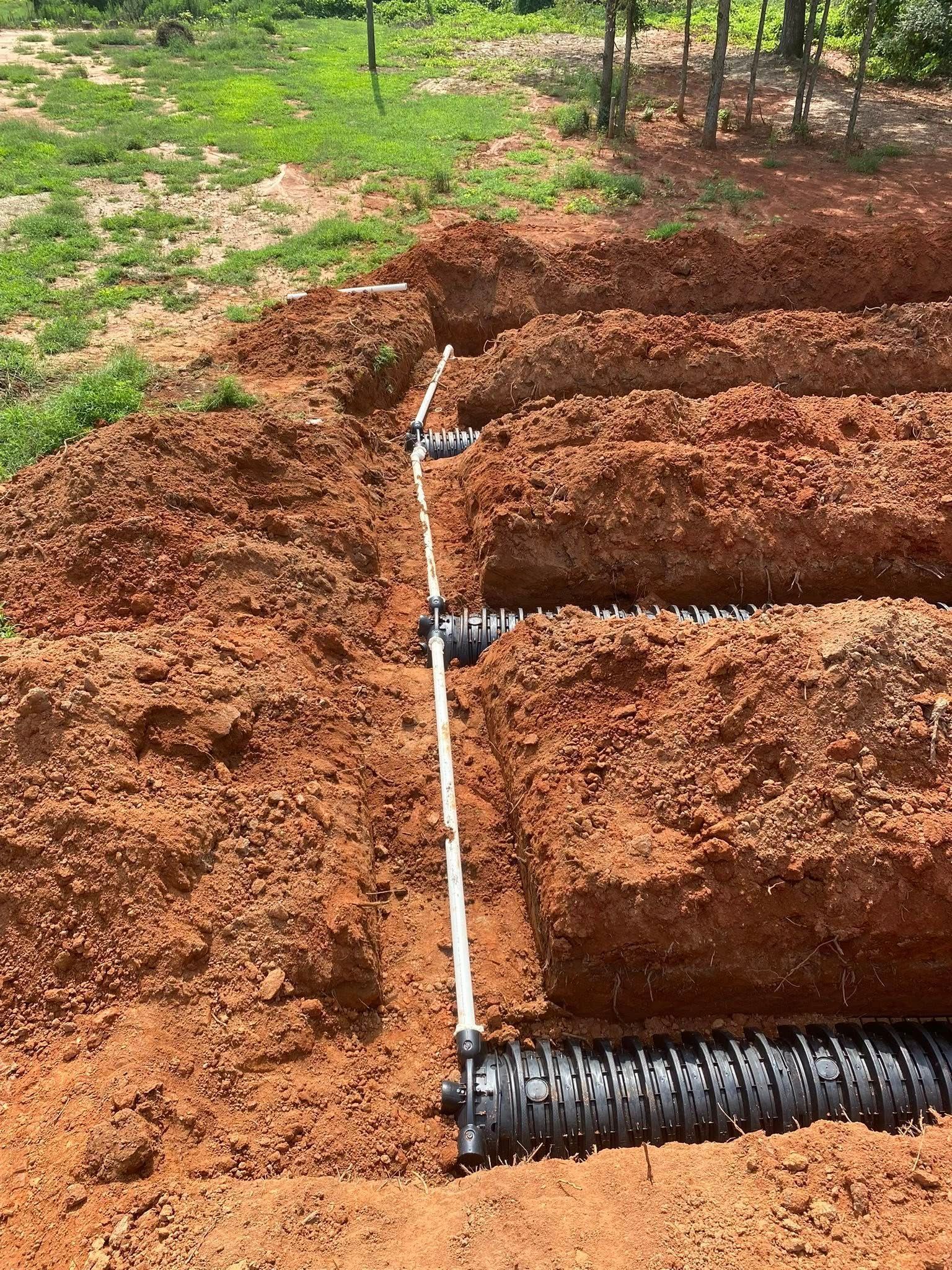 Trenches with perforated pipes for a drainage system in red soil.