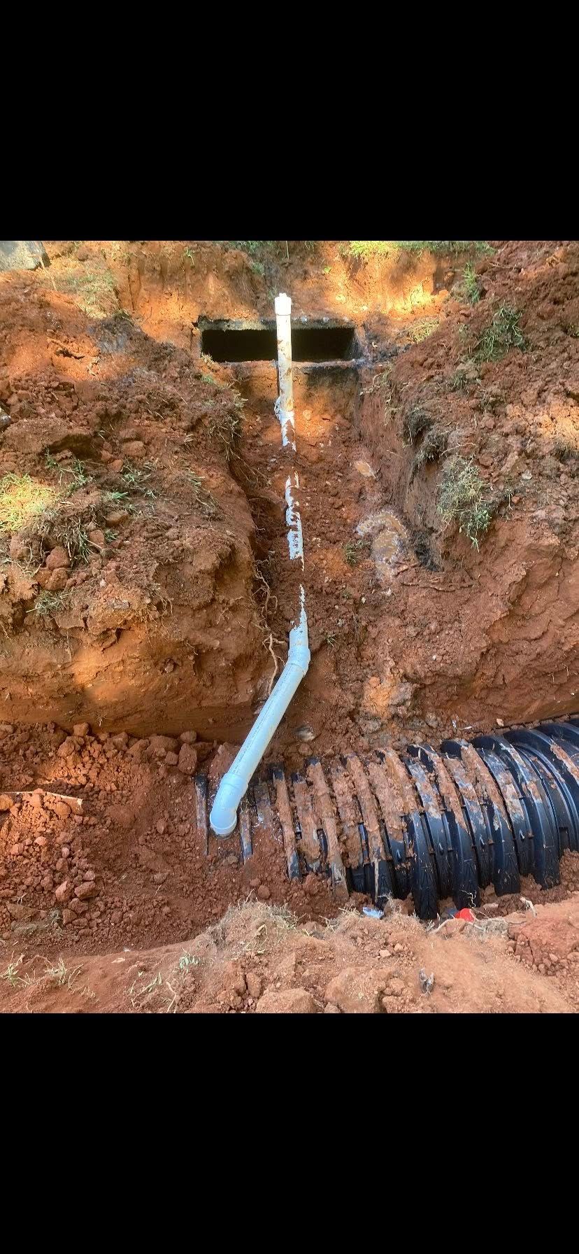 Drainage system installation in brown dirt trench, showing pipes connected.