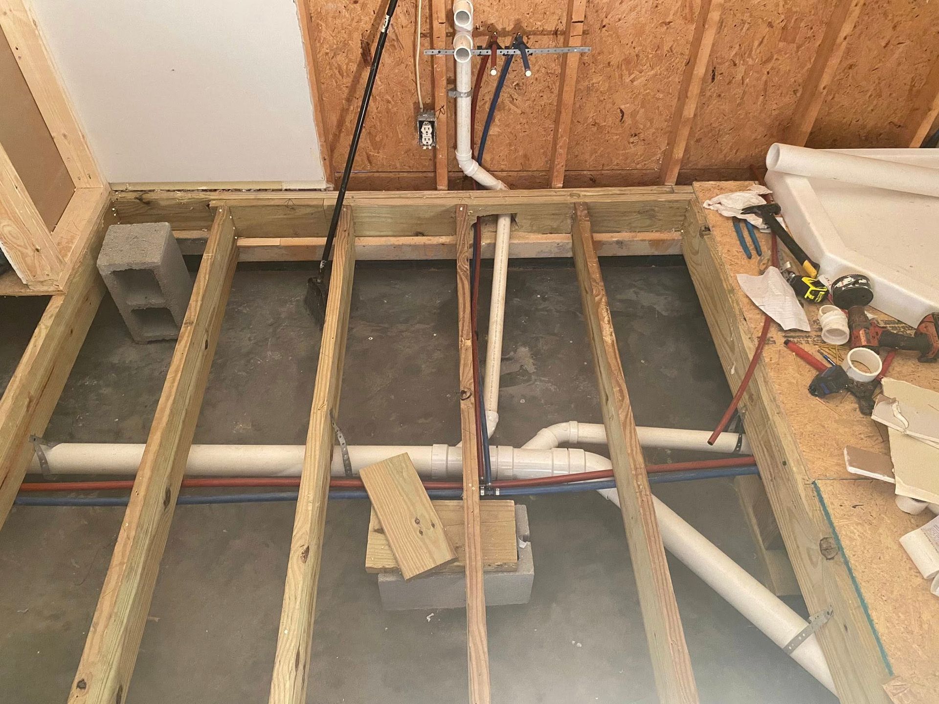 Framed wooden floor with plumbing pipes and concrete subfloor; construction site.