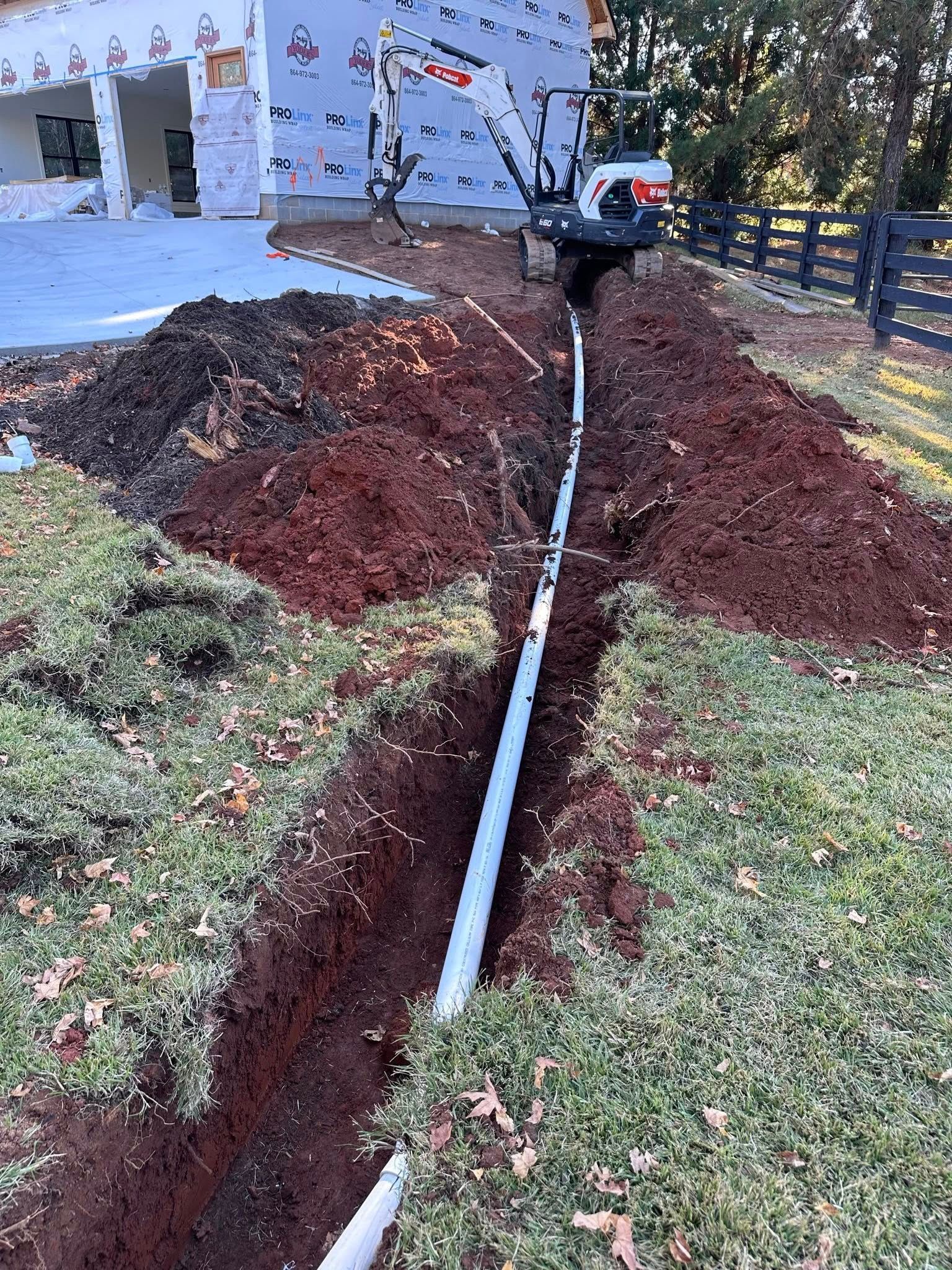 An excavator digs a trench for a drainage pipe near a house under construction.
