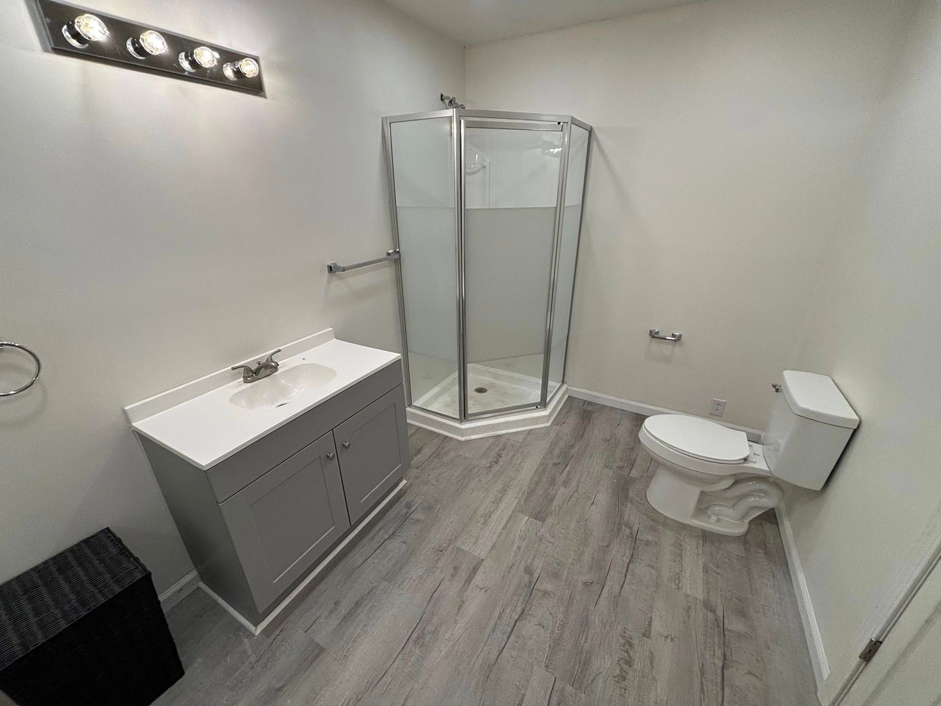 Bathroom with a gray vanity, glass shower, and toilet on gray wood-look flooring.