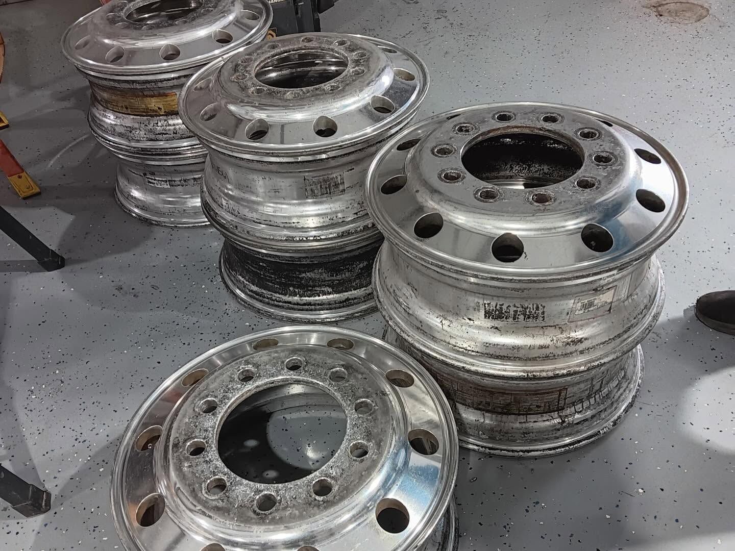 Stacked silver truck wheel rims on a workshop floor, with scratches and rust spots.