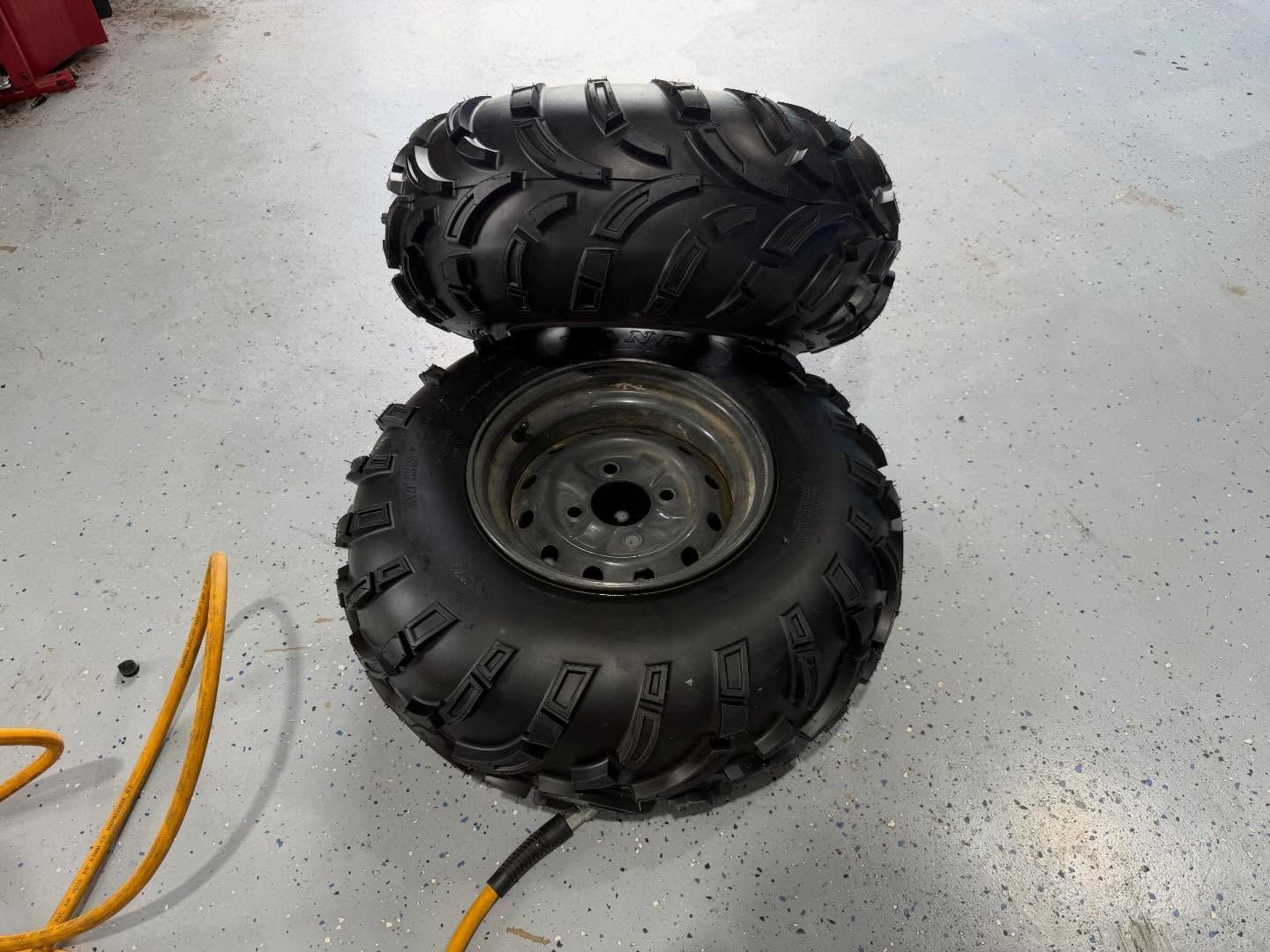 Two black off-road tires on a gray garage floor, one stacked atop the other