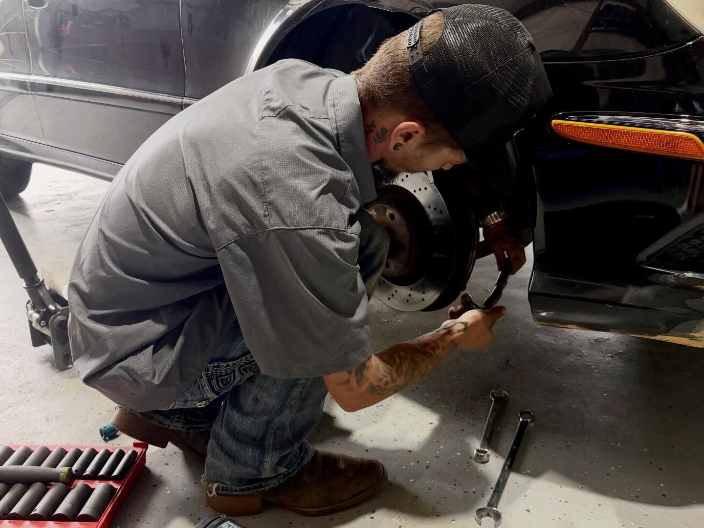 Mechanic in gray shirt repairing a car’s brake assembly in a garage