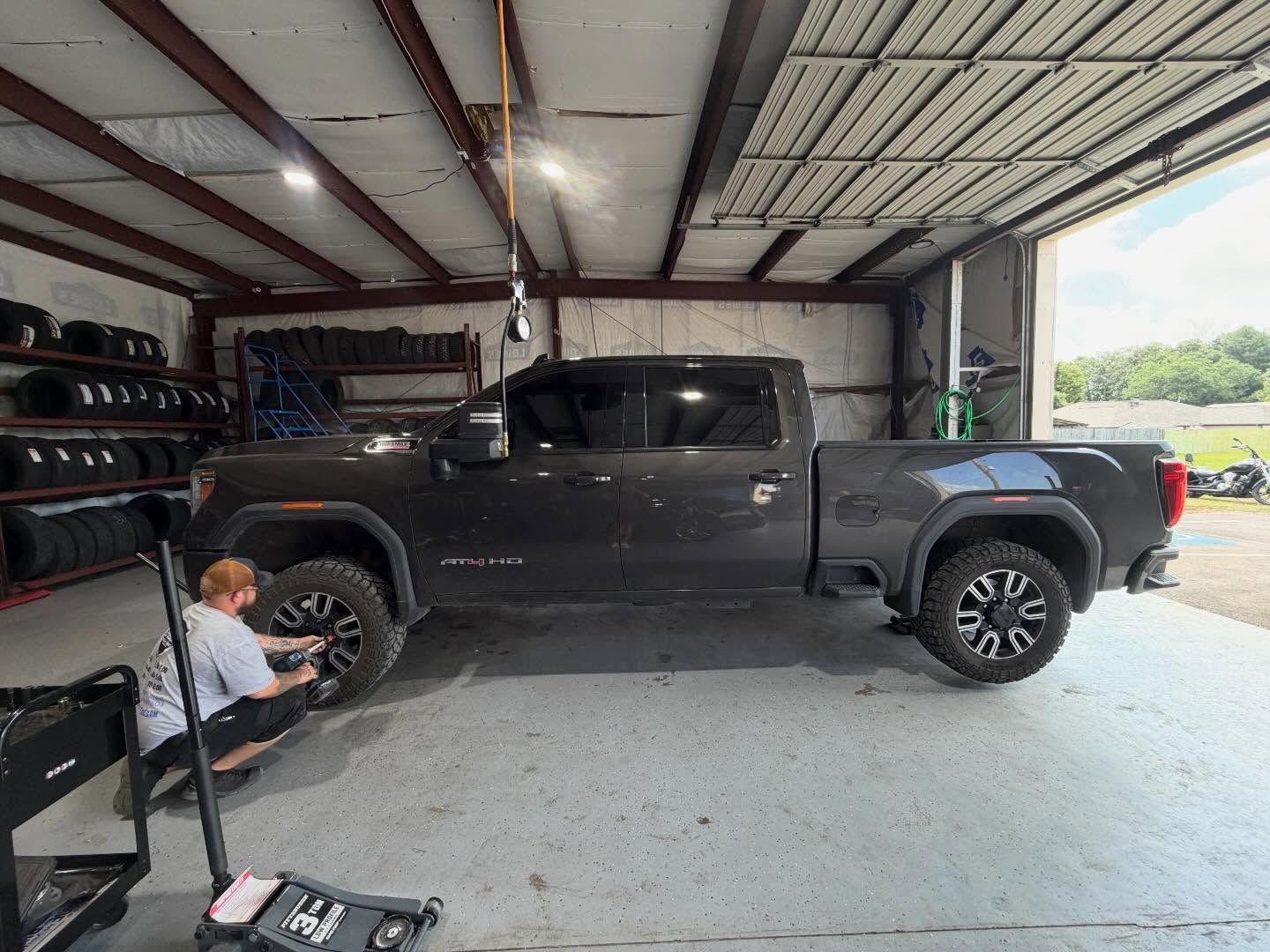 Black pickup truck in a garage with a person working near the front wheel.