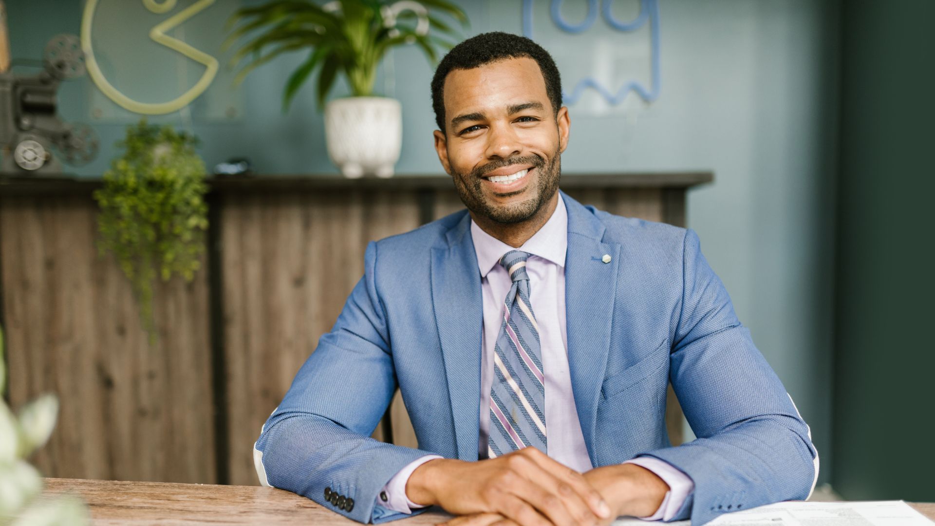 Smiling man in a blue suit seated at a desk in an office setting