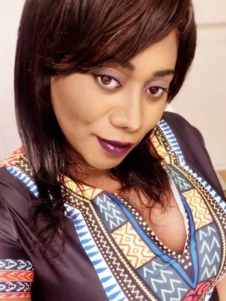 A woman wearing a colorful shirt and purple lipstick is taking a selfie.