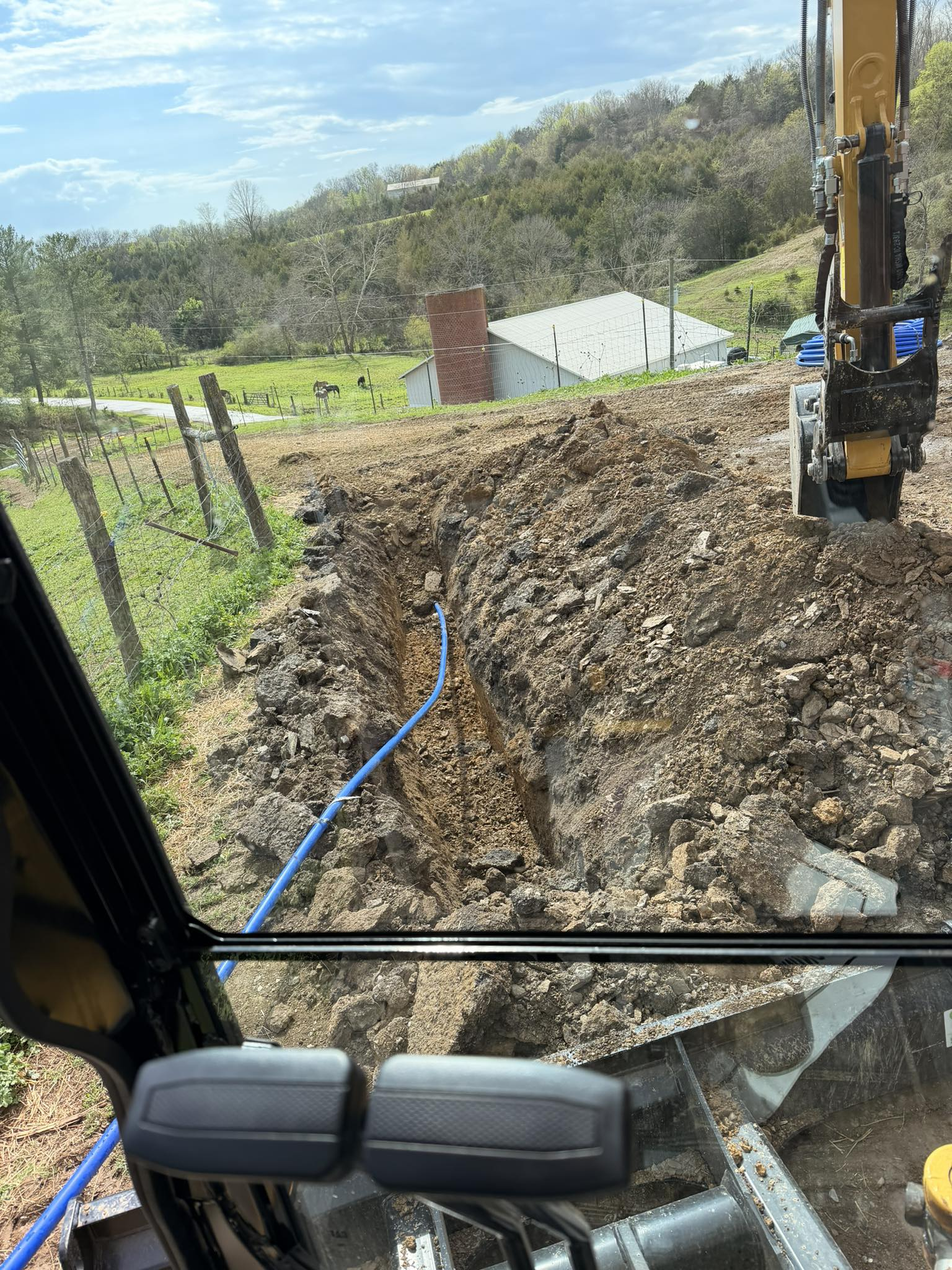Excavator beside a dirt pile with a blue hose on a hillside construction site