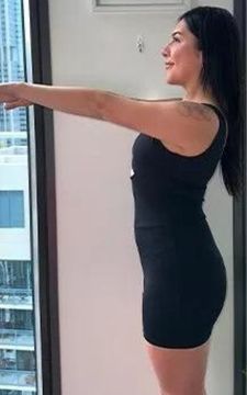 Woman in black athletic wear stands with arms outstretched near a window.