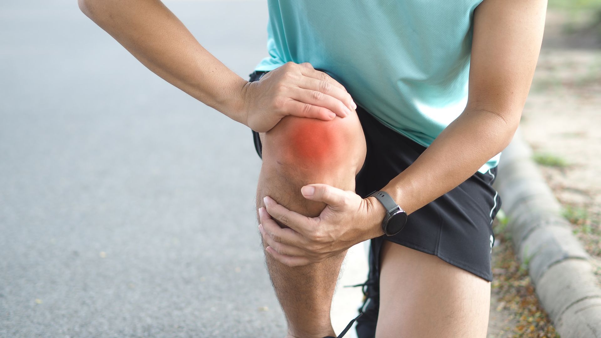 Man holding knee in pain, highlighted in red, on a road.
