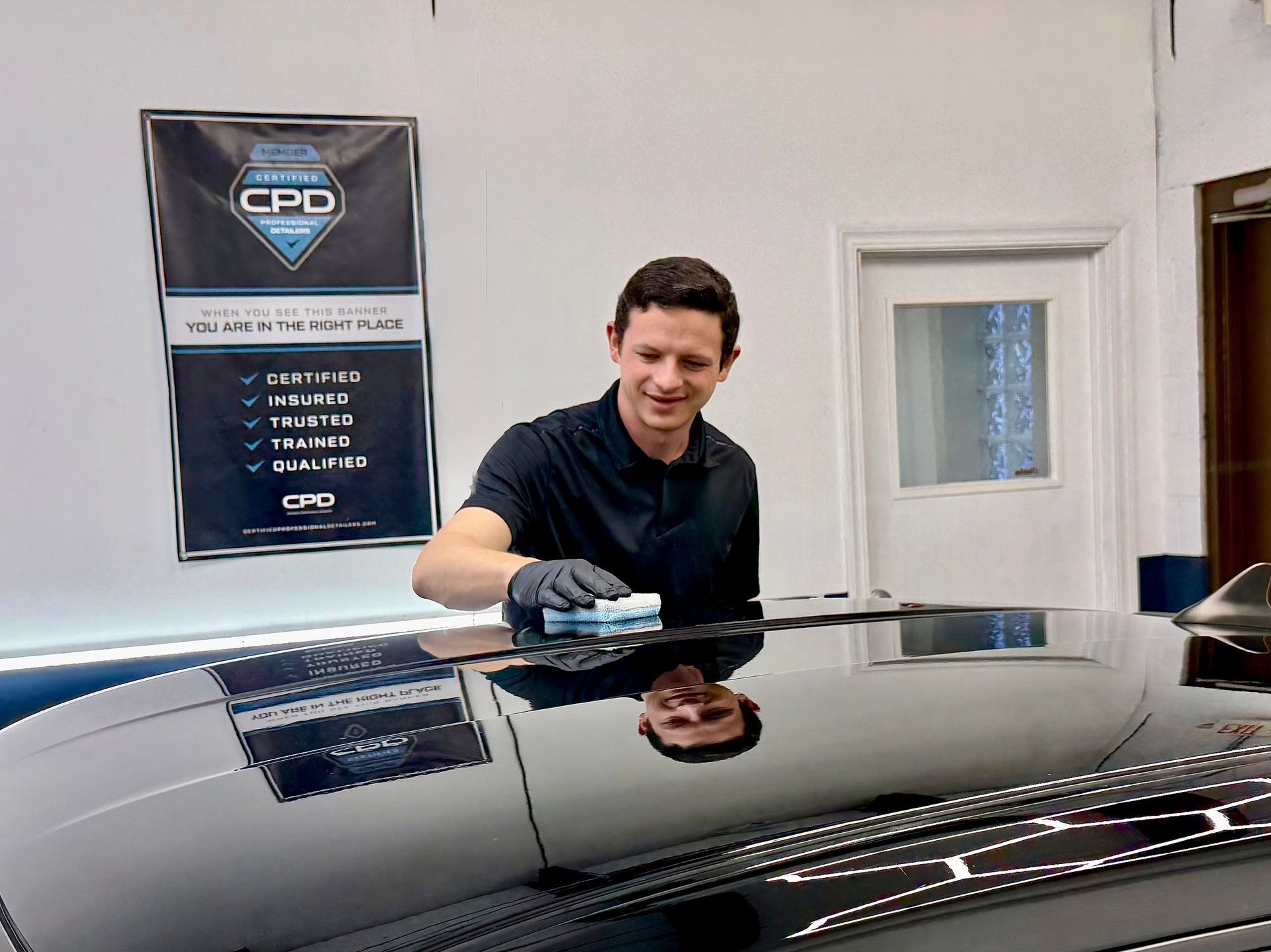 A person wearing black gloves and a shirt with a logo applies a product to a blue applicator sponge in a garage.