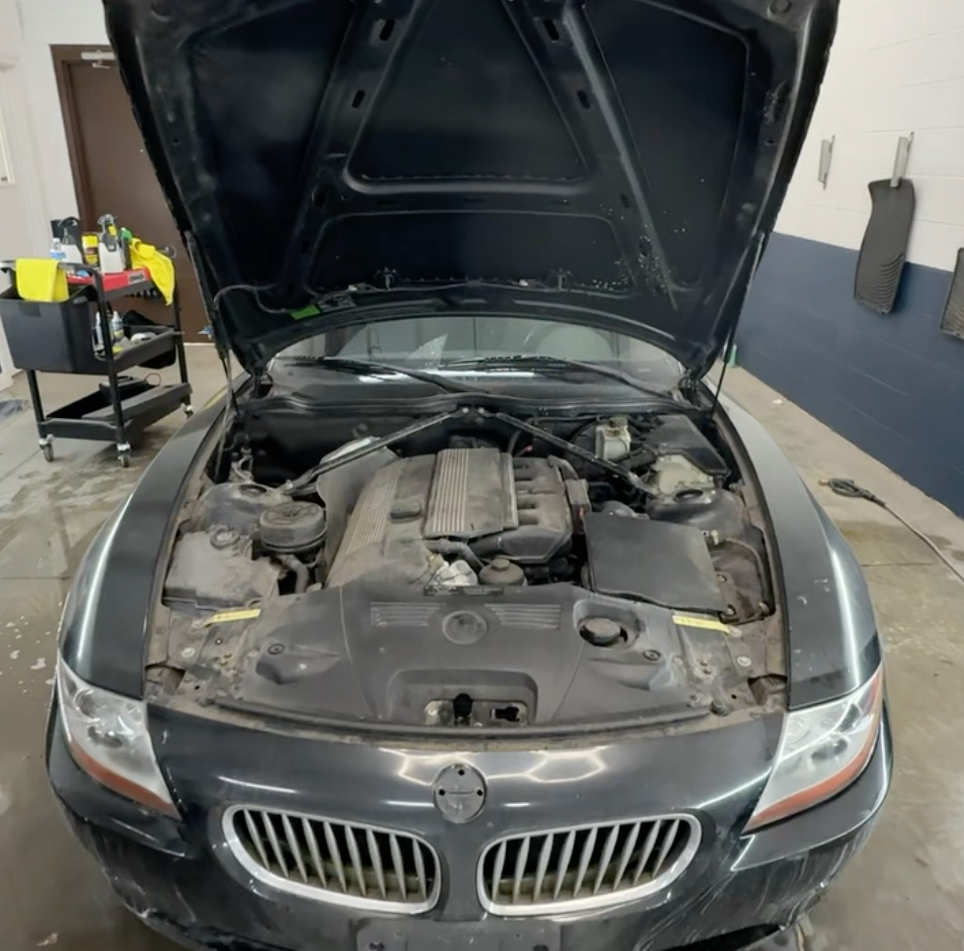 Black BMW in a garage with the hood open, showing the engine bay.