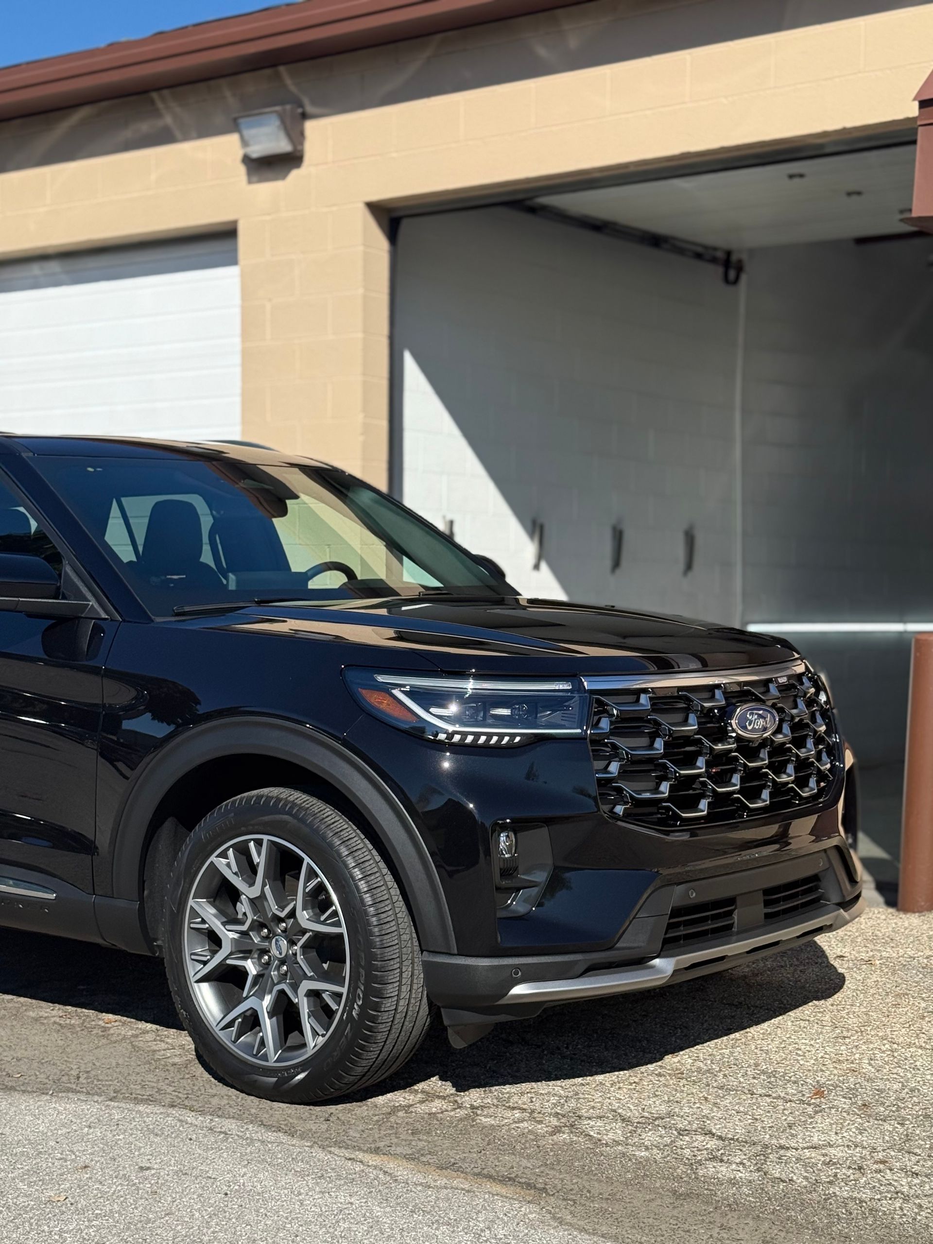 A black Ford Explorer SUV parked on a gravel surface in front of a building with two open garage bays.