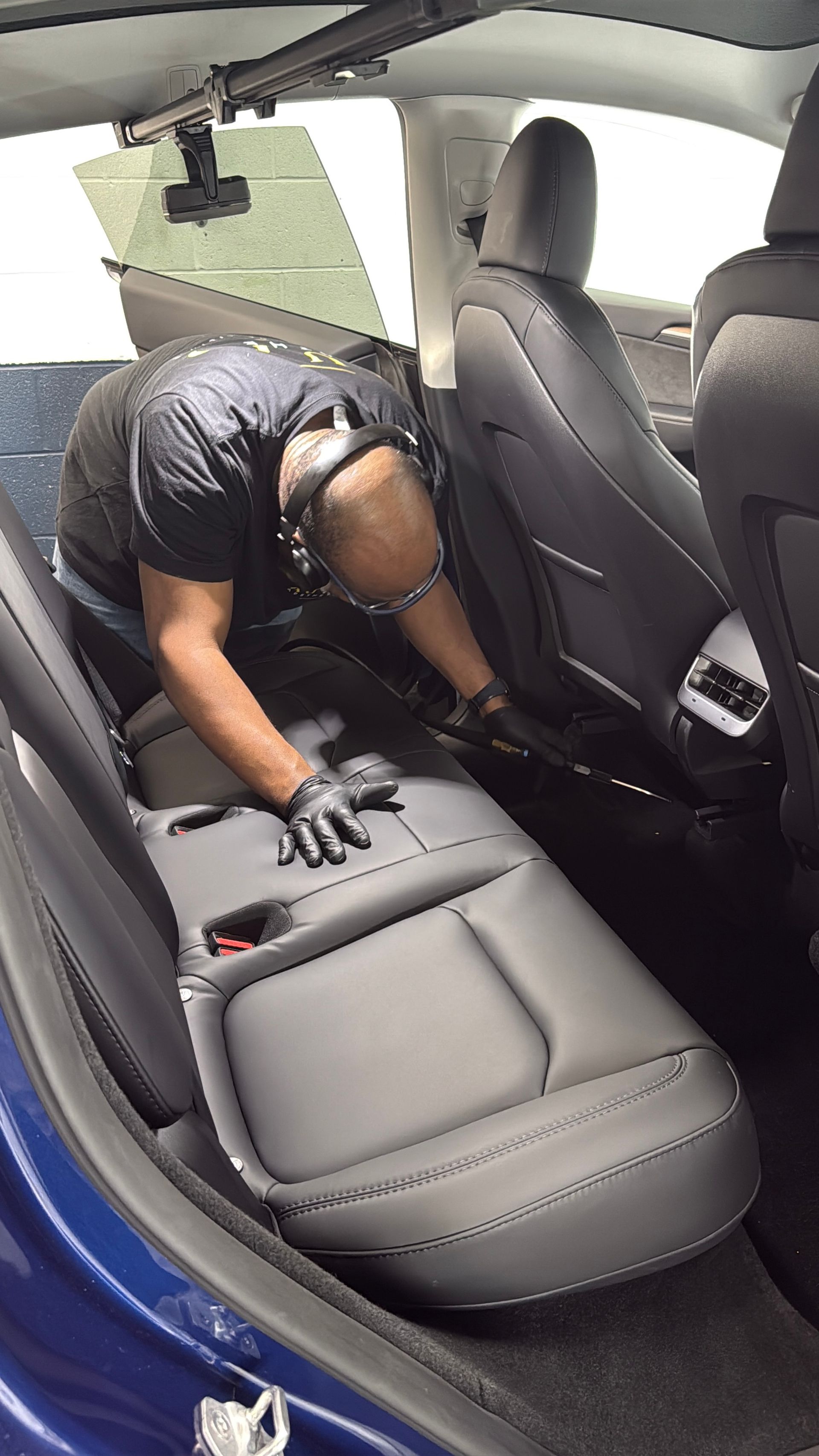 A technician in a black uniform standing next to a bright red Toyota Prius in an auto detailing shop.