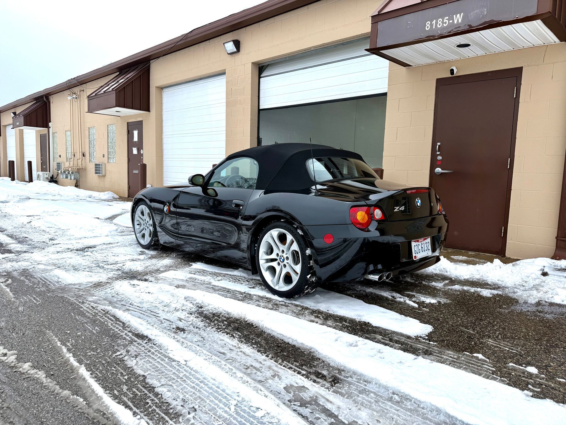 Black convertible car parked in front of a building with snowy ground.