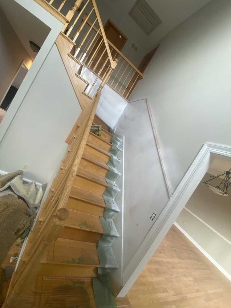 Wooden staircase with handrail in a two-story home, plastic covering stairs, light walls, and wooden floors.