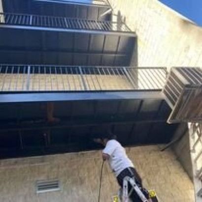 Person on ladder working on the underside of a building's balcony.