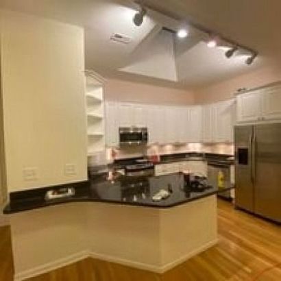 Kitchen with white cabinets, black countertop, island, stainless steel refrigerator, and hardwood floors.