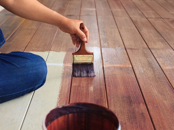 Person applying stain to wooden floor with a brush.