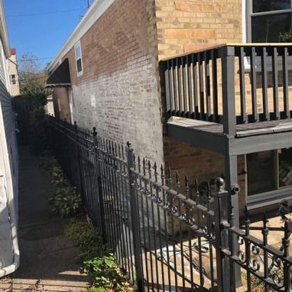 Narrow alleyway with black wrought-iron fence, brick building, and wooden deck.