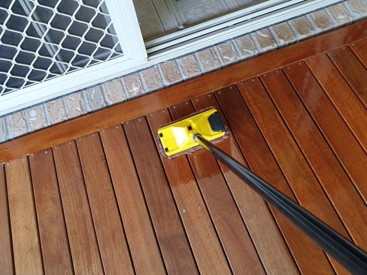 Yellow applicator applying stain to a wooden deck next to a window.