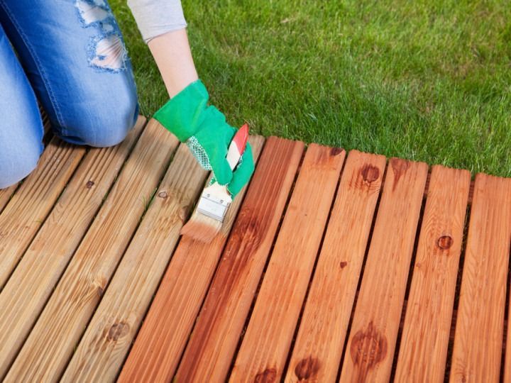 Person staining wooden deck with paintbrush.