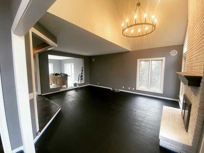 Empty living room with dark floor, gray walls, white trim, and a chandelier.